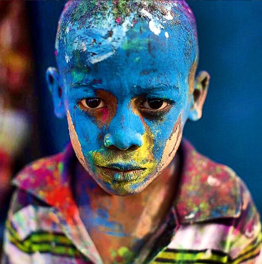 Portrait of a child with vivid blue face paint and multicolor clothing.